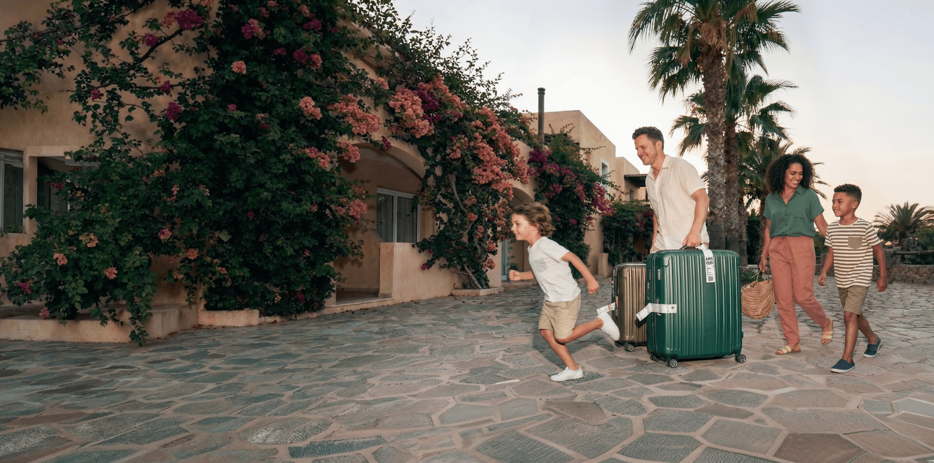 Gezin loopt met rolkoffers over een pad naar een vakantiewoning, terwijl een kind vooruit rent