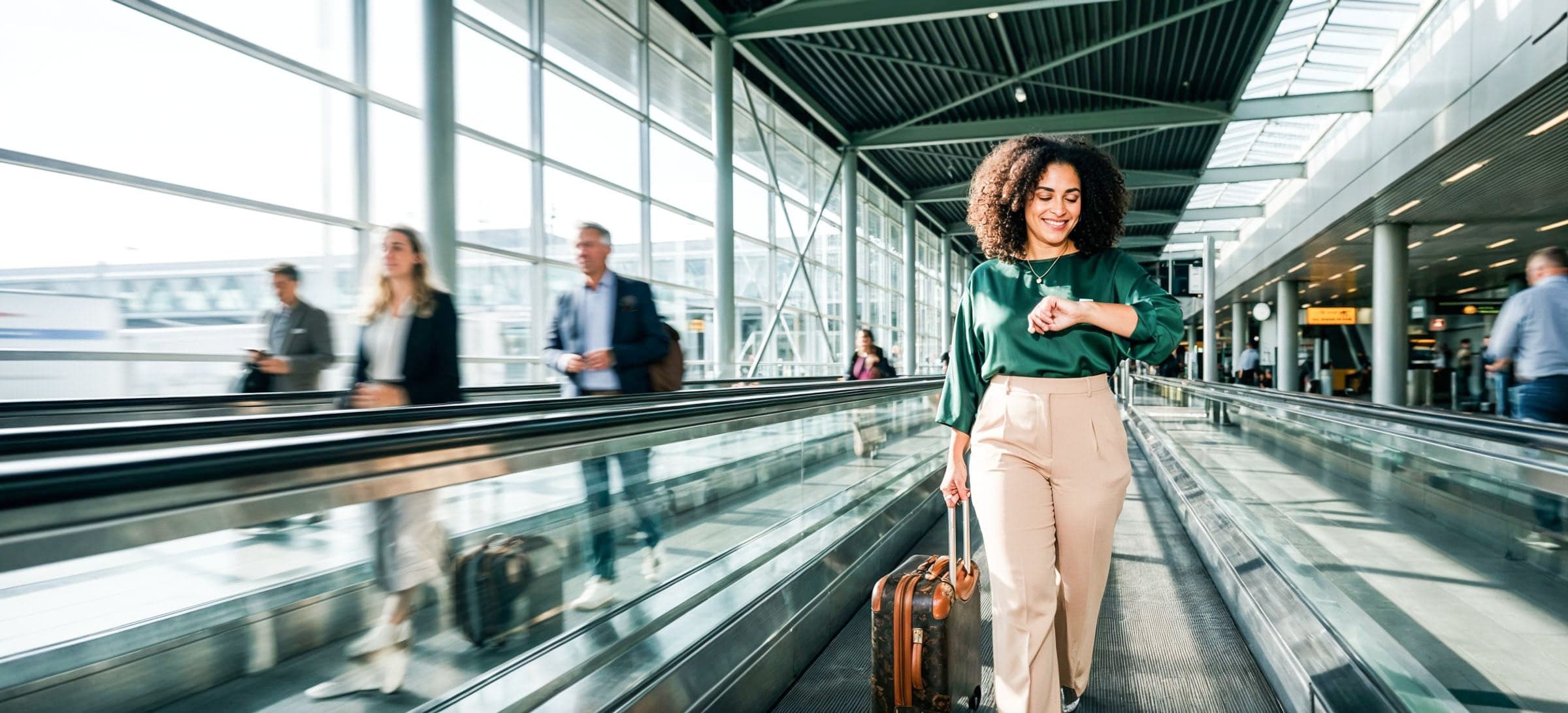 Zakelijke reiziger loopt met een rolkoffer over een loopband in een moderne luchthaven en controleert de tijd