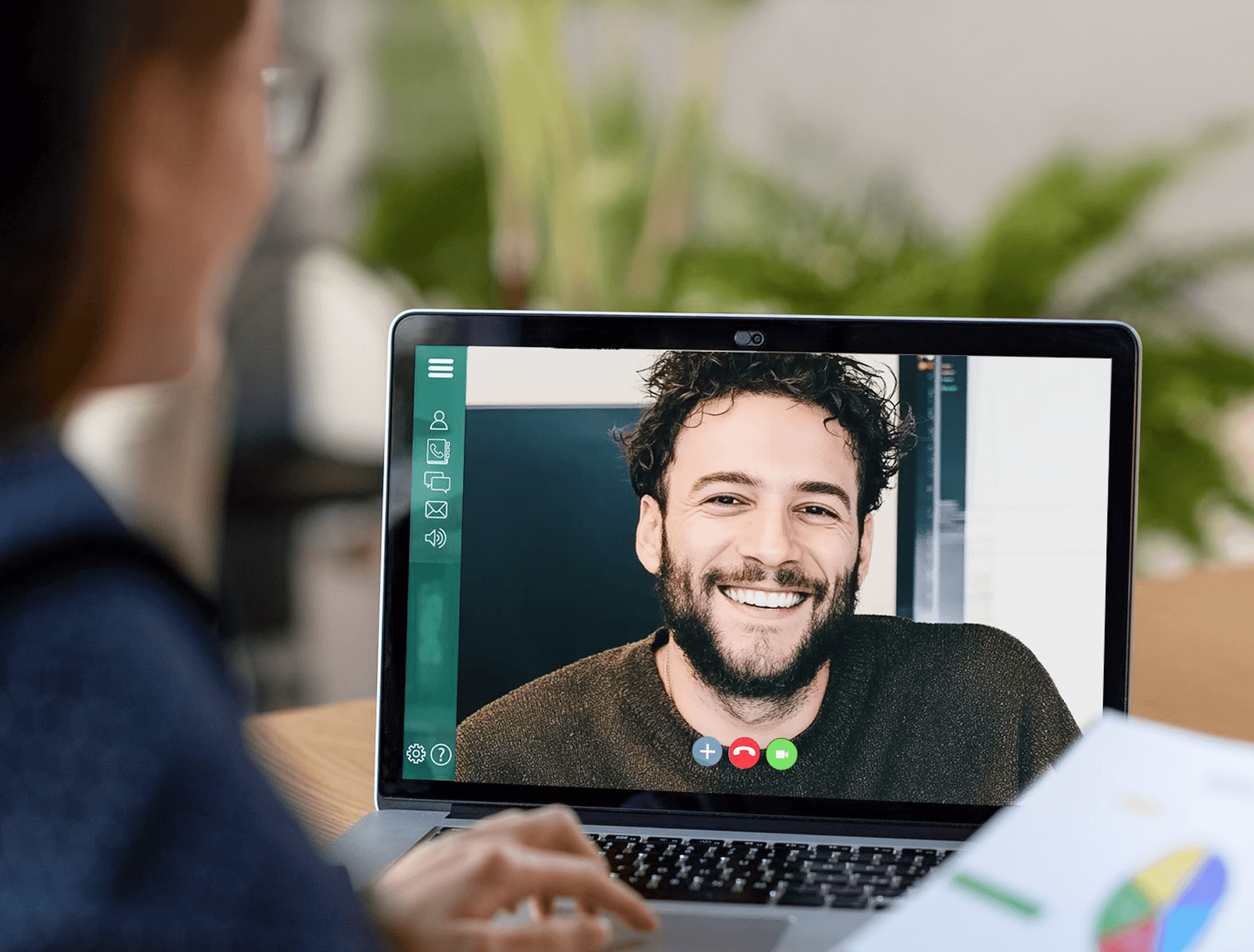 Persoon neemt deel aan een videogesprek op een laptop, terwijl een document met grafieken zichtbaar is op de voorgrond